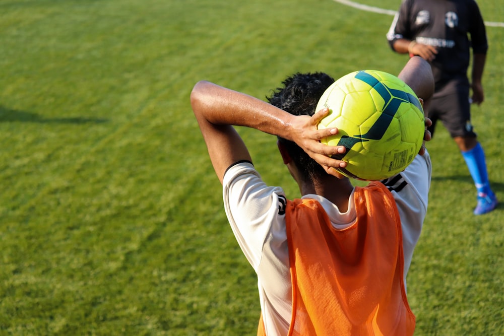 homem na camisa da camisa laranja e calções brancos segurando a bola de futebol amarela