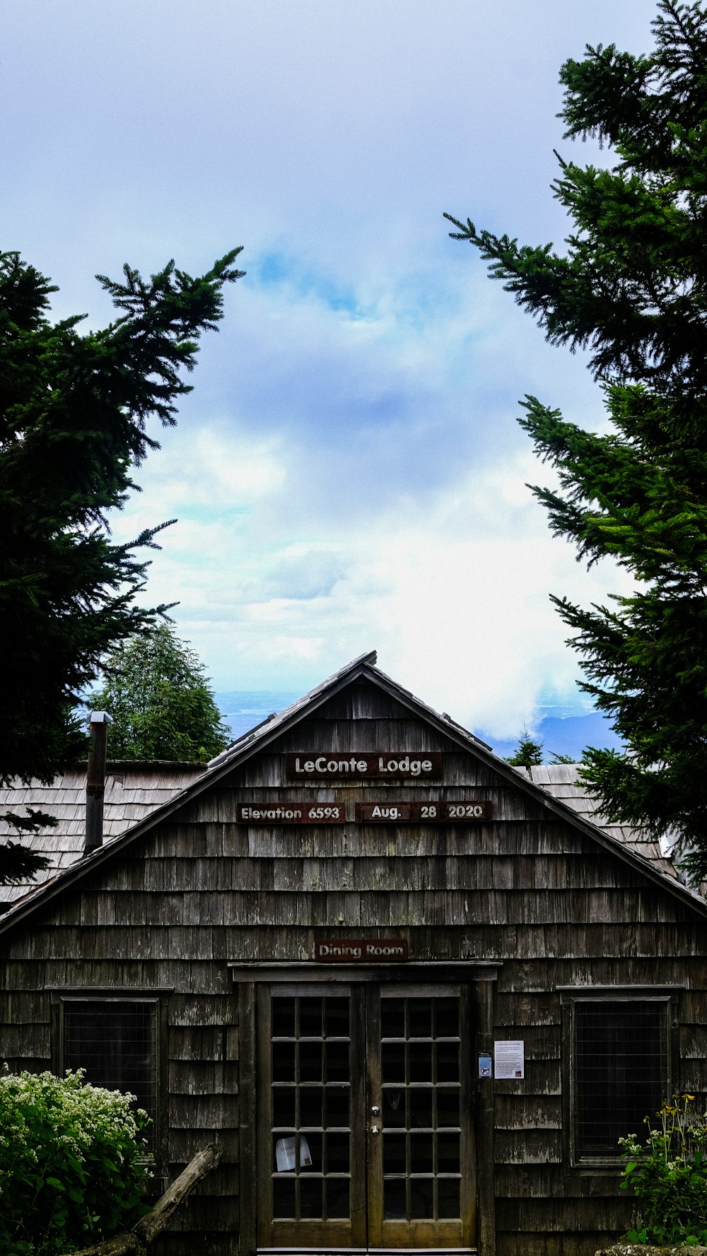 Braunes Holzhaus in der Nähe grüner Bäume unter weißen Wolken tagsüber