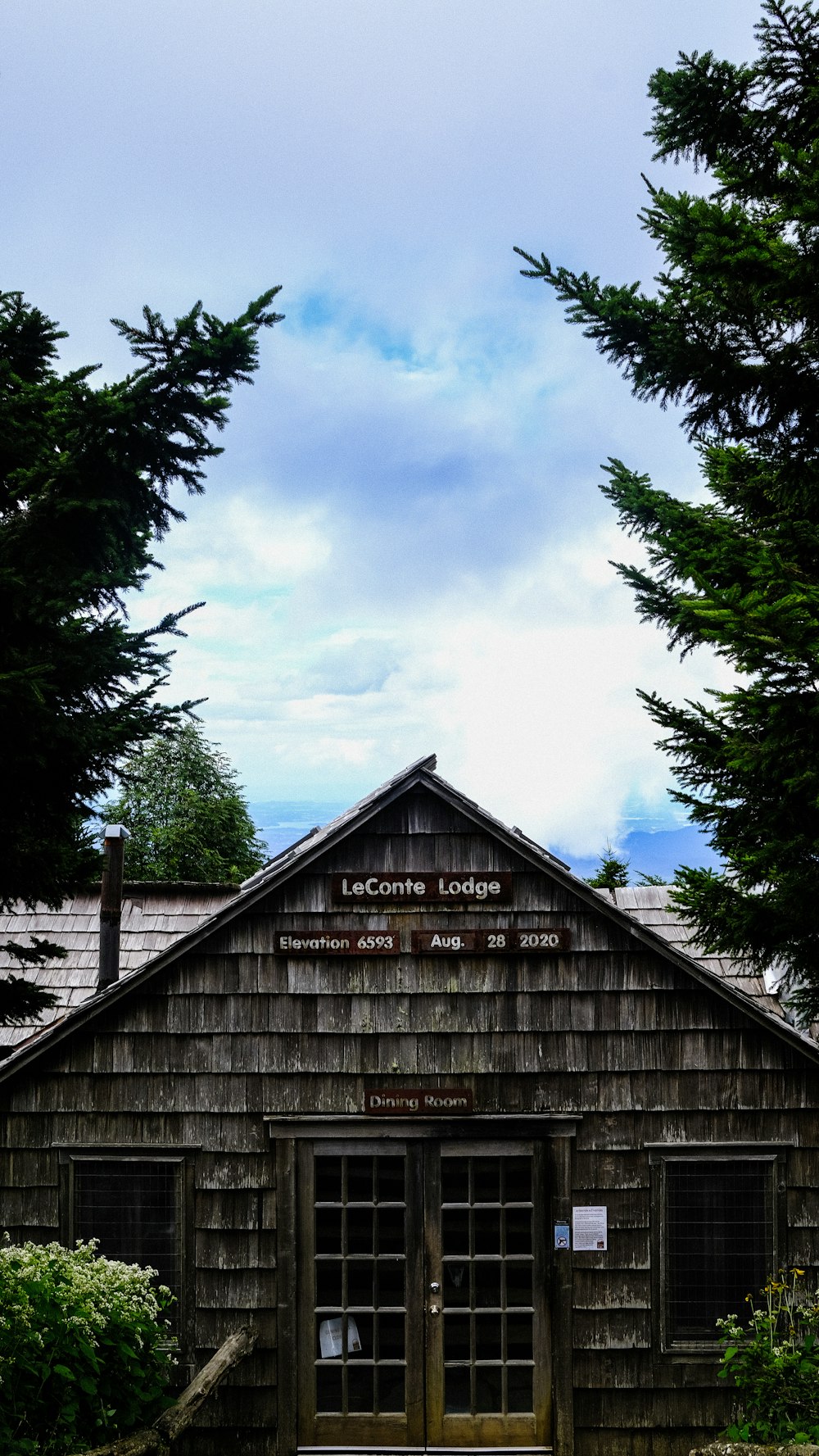 casa de madera marrón cerca de árboles verdes bajo nubes blancas durante el día