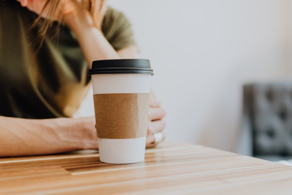 woman in green shirt holding white and black disposable cup