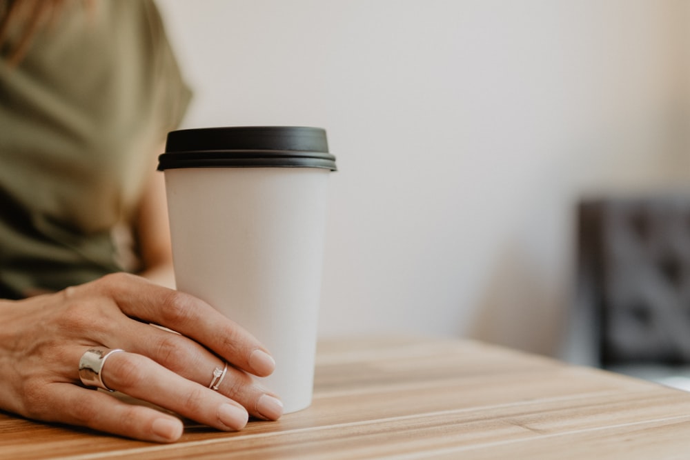 Persona che tiene la tazza usa e getta bianca