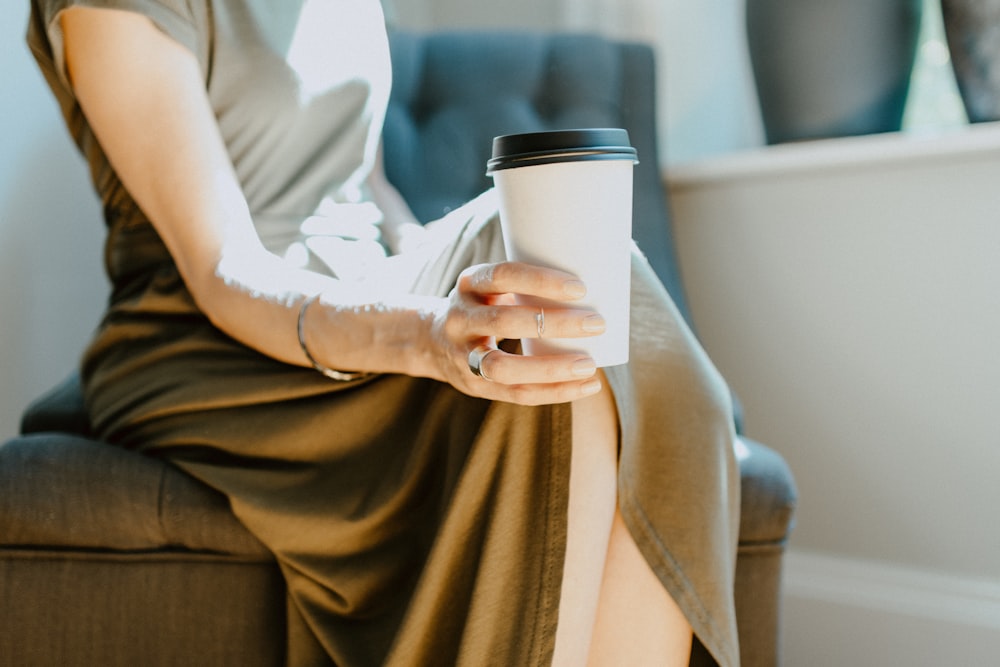 woman in white shirt and brown skirt holding white cup