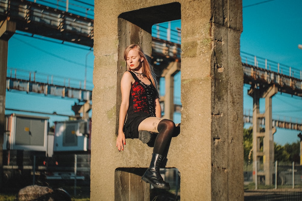 woman in red tank top and black shorts sitting on black metal post during daytime