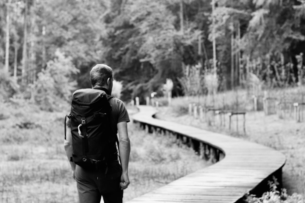 Foto in scala di grigi di donna che cammina sul ponte di legno