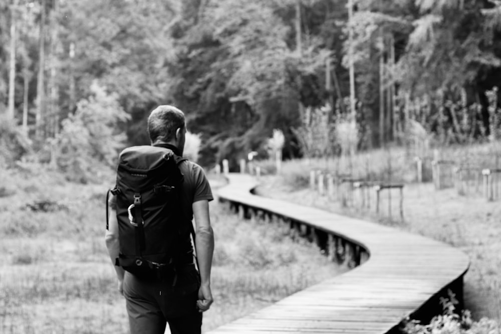 grayscale photo of woman walking on wooden bridge