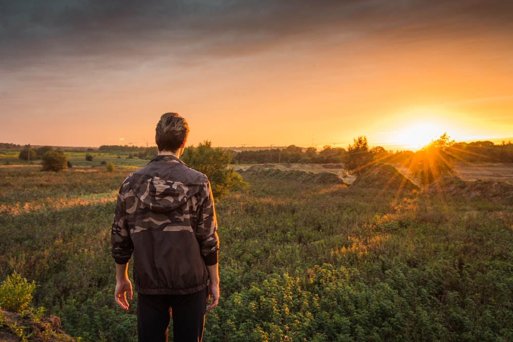 man in gray and black camouflage jacket standing on green grass field during sunset