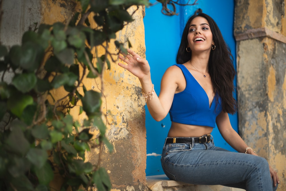 woman in blue tank top and blue denim jeans leaning on brown wall