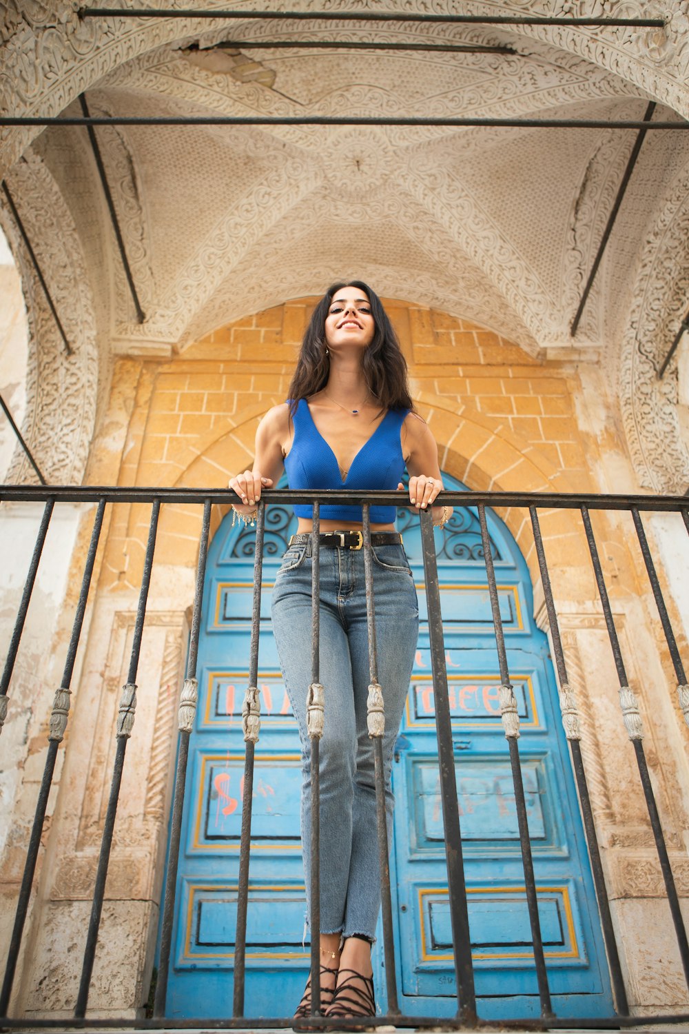 woman in blue tank top and blue denim jeans standing on brown wooden staircase