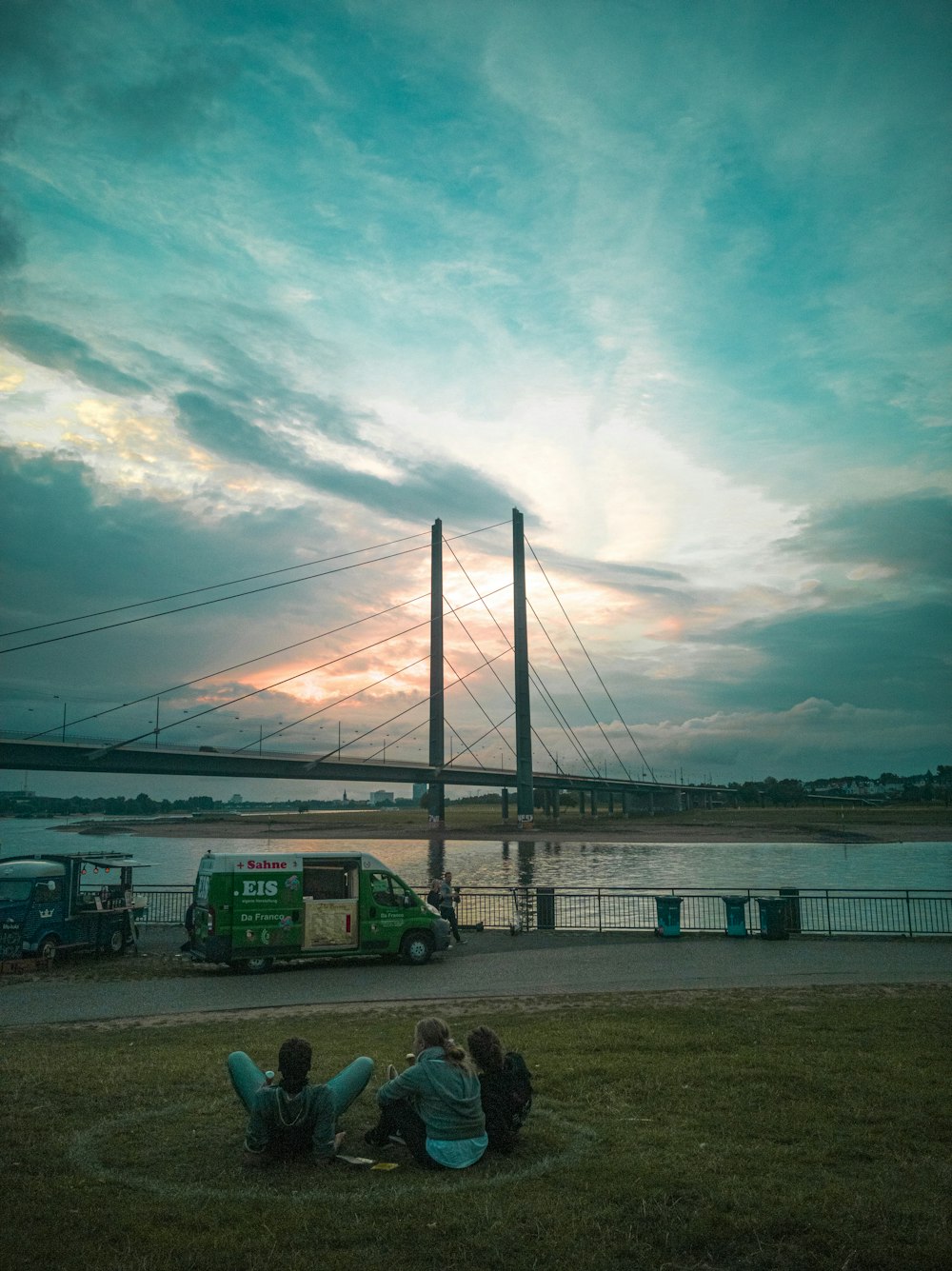 people sitting on bench near bridge under cloudy sky during daytime