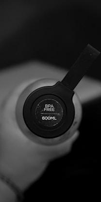 A close-up view of the top of a water bottle, featuring a black cap with a label indicating it is BPA-free and has a capacity of 600ML. The bottle is being held in a hand.