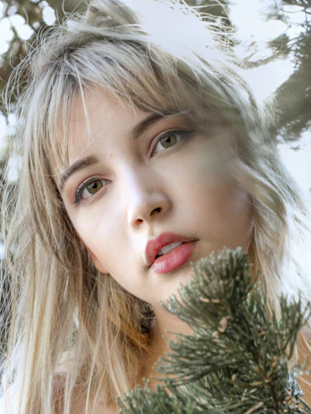 A close-up portrait of a woman with natural makeup, smiling gently against a blurred garden background.