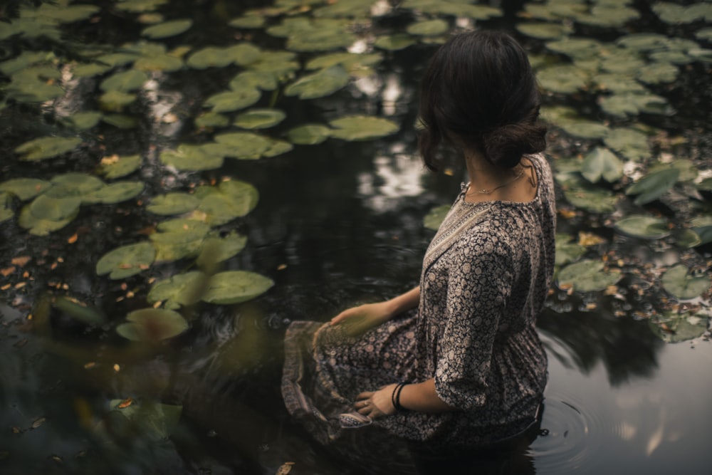 Frau in schwarz-weißem Blumenkleid sitzt auf dem Wasser
