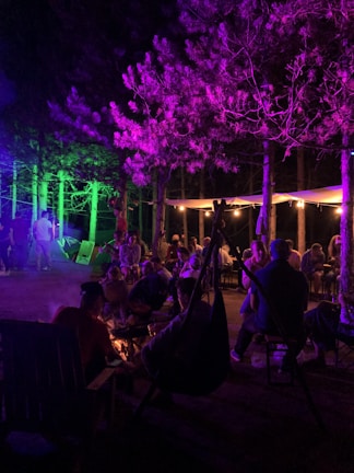 Evening community meet-up with members chatting around a bonfire under string lights.