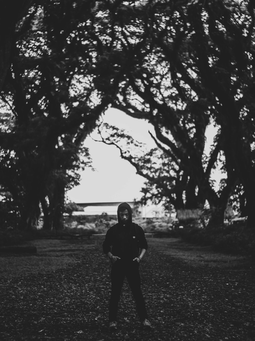 grayscale photo of man in black jacket standing near trees