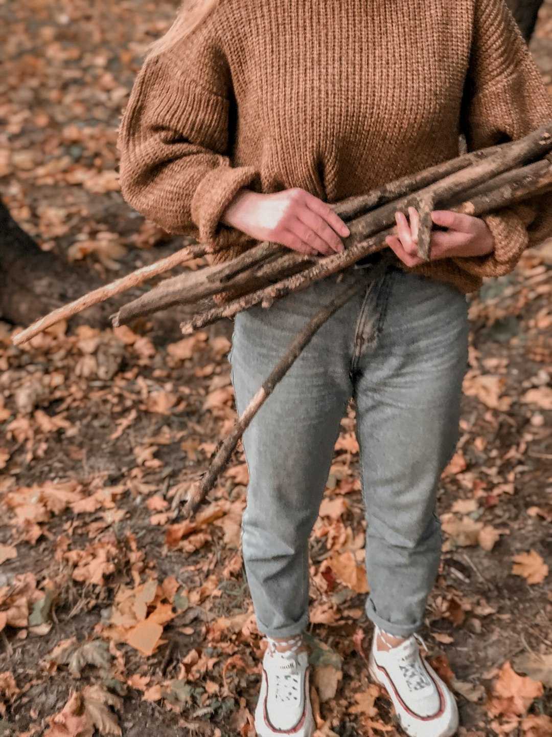 man in brown sweater and blue denim jeans holding brown stick