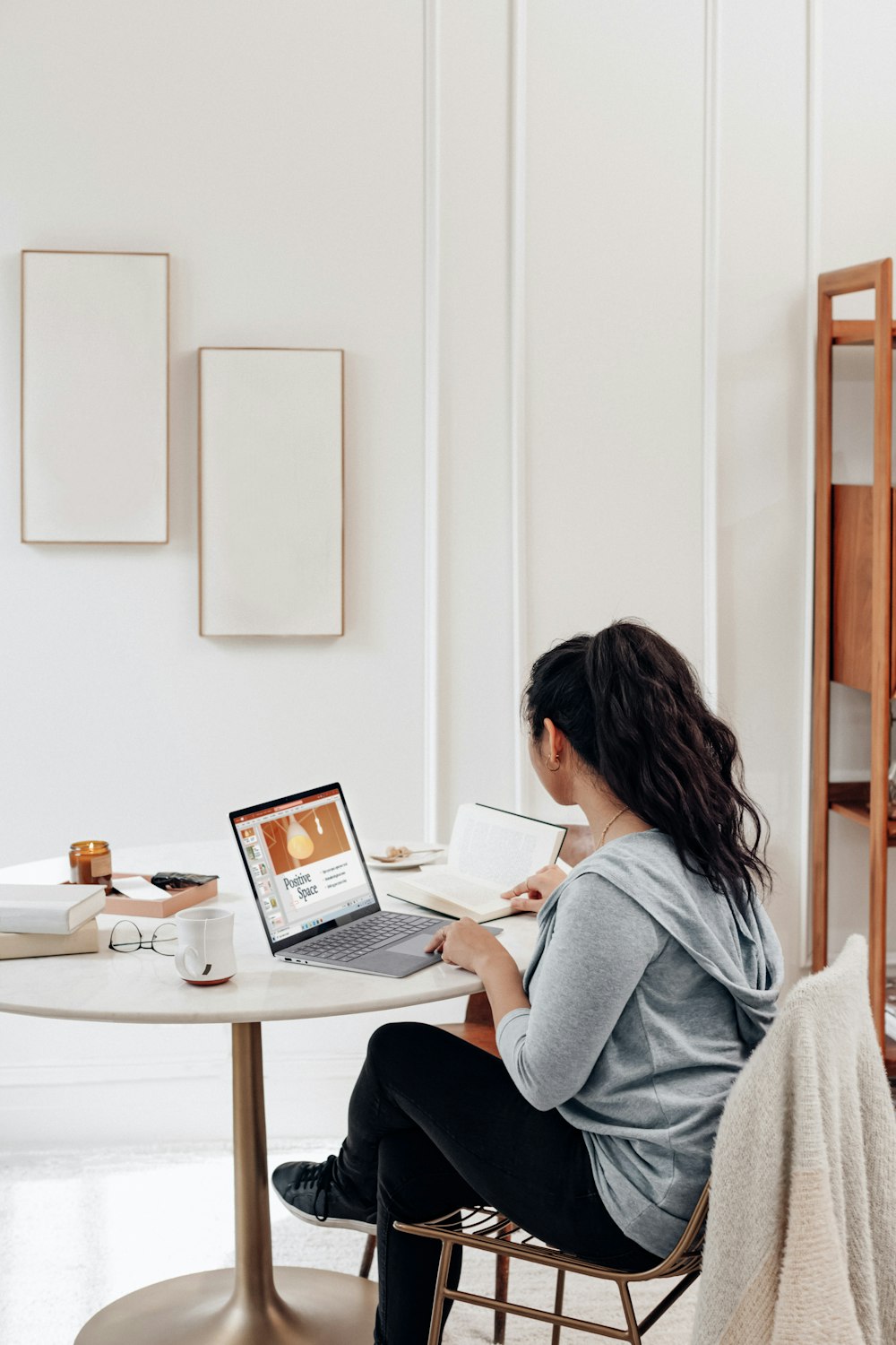 Mujer con suéter gris usando MacBook Air sobre mesa blanca