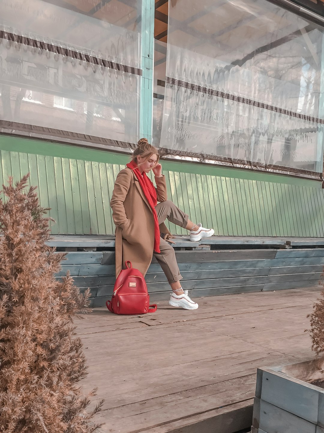 woman in brown coat and red pants sitting on brown brick floor