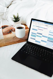 person holding white ceramic mug in front of black laptop computer