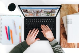 A writer typing on a laptop surrounded by notes and coffee.