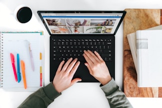 A friendly person typing on a laptop with books and a coffee cup nearby.
