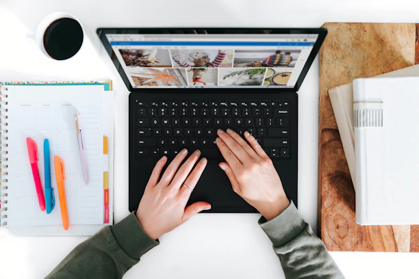 Close-up of hands typing on a keyboard with educational books and a coffee cup nearby.