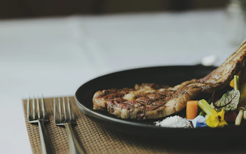 A close-up of a perfectly charred ribeye steak plated with fresh herbs and a side of smoky sauce.
