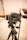 A professional camera mounted on a tripod is set up in what appears to be a photography studio. The background is slightly out of focus, with some photography equipment visible, including light stands and softboxes.