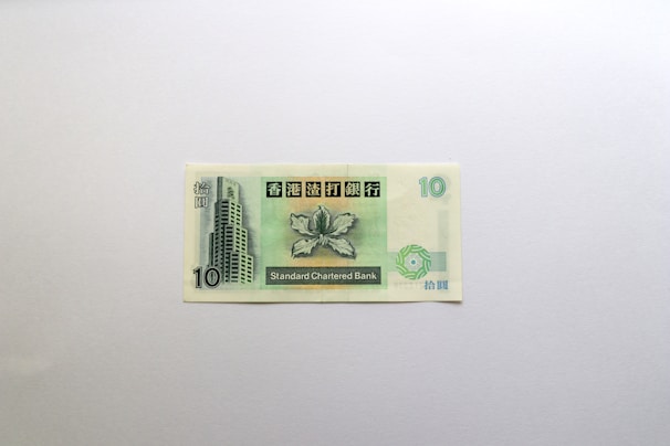 A banknote from Standard Chartered Bank, featuring a prominent building design and decorative leaf motif. The number 10 is displayed in two corners, with Chinese characters printed above.