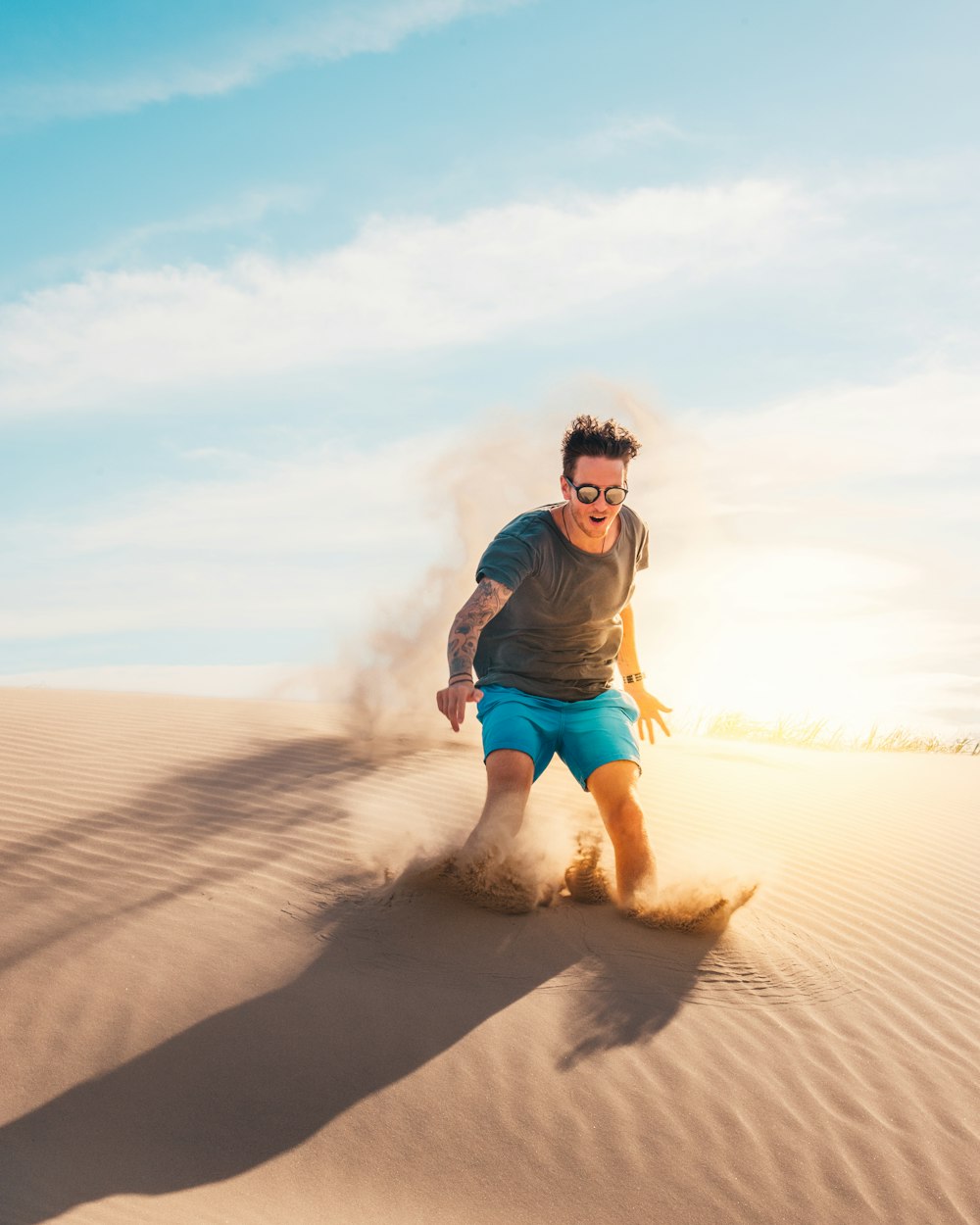 Mann in blau-schwarzer Jacke und orangefarbenen Shorts sitzt tagsüber auf Sand