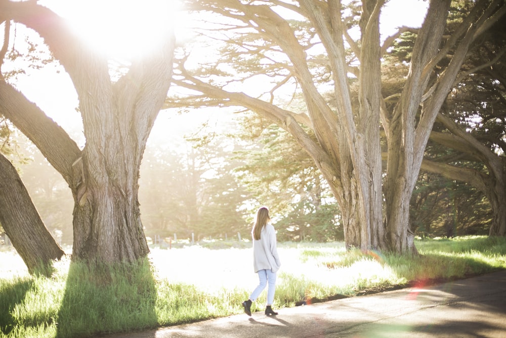 woman in white long sleeve shirt and black pants walking on pathway between trees during daytime