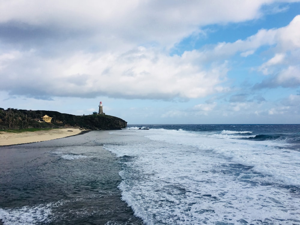 white and black lighthouse on seashore under white clouds and blue sky during daytime