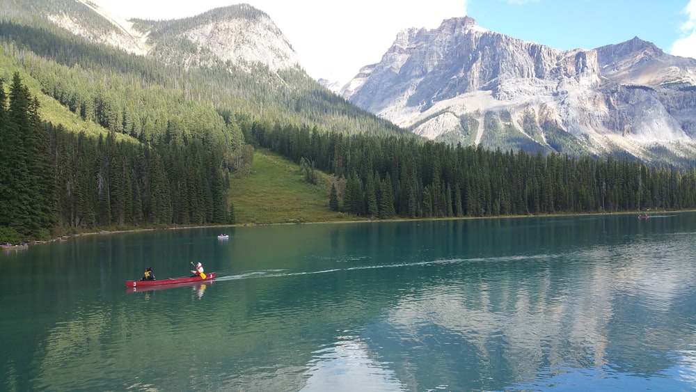 person riding on red boat on lake near green trees and mountain during daytime