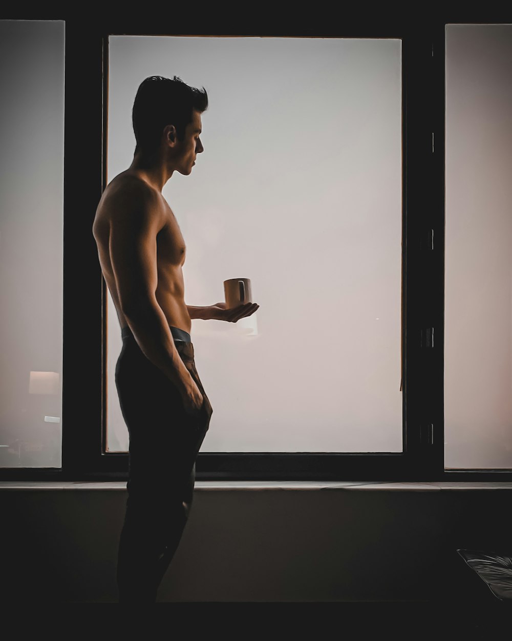 topless man in black pants holding black ceramic mug