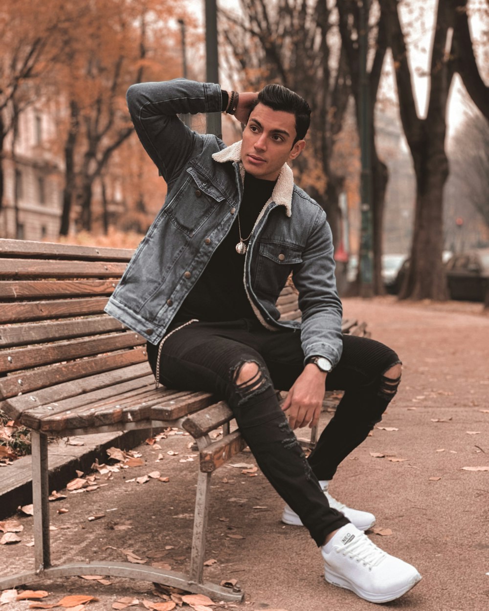 man in black leather jacket sitting on brown wooden bench during daytime