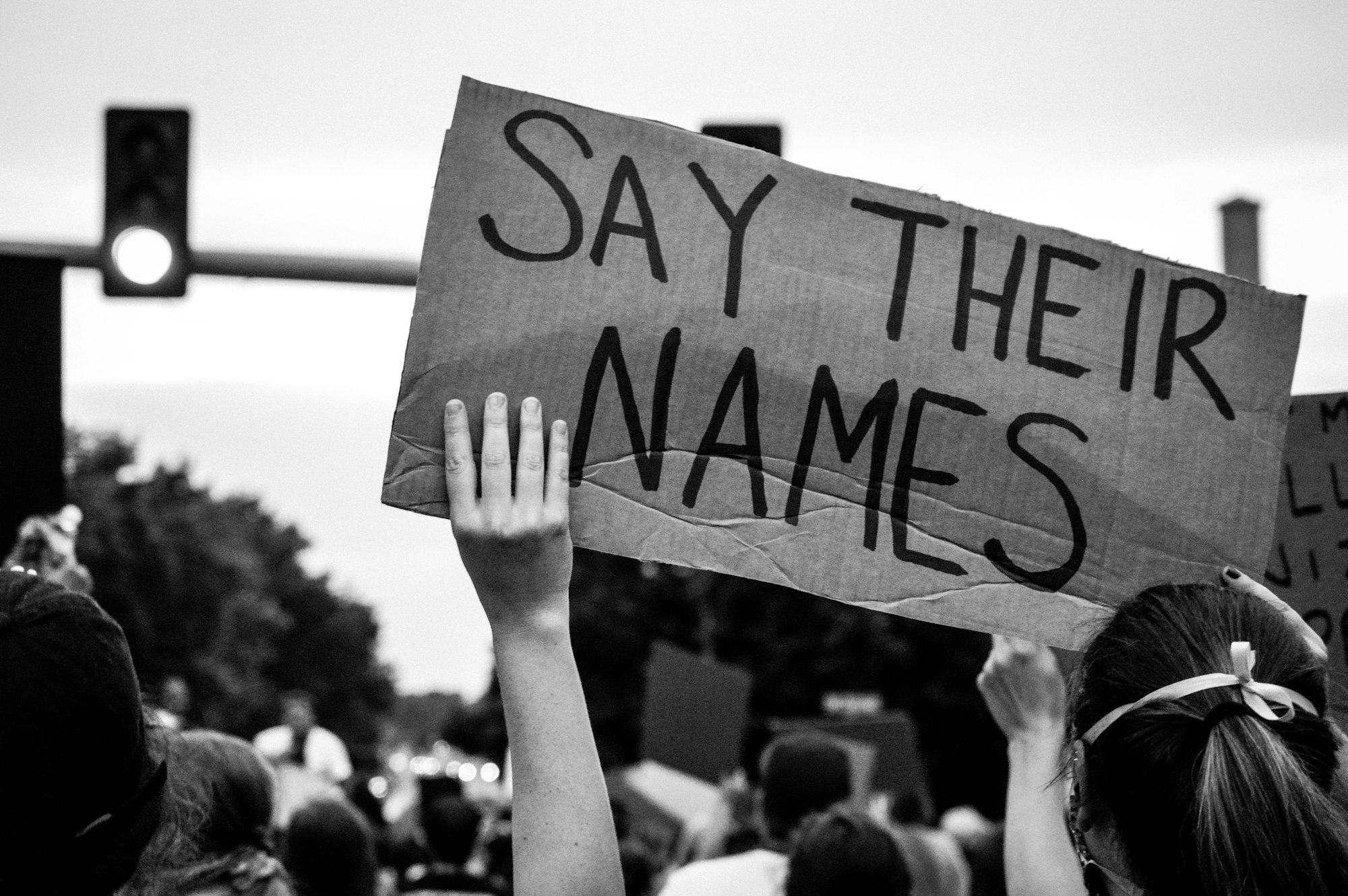 black lives matter protest, holding a sign that says "say their names"