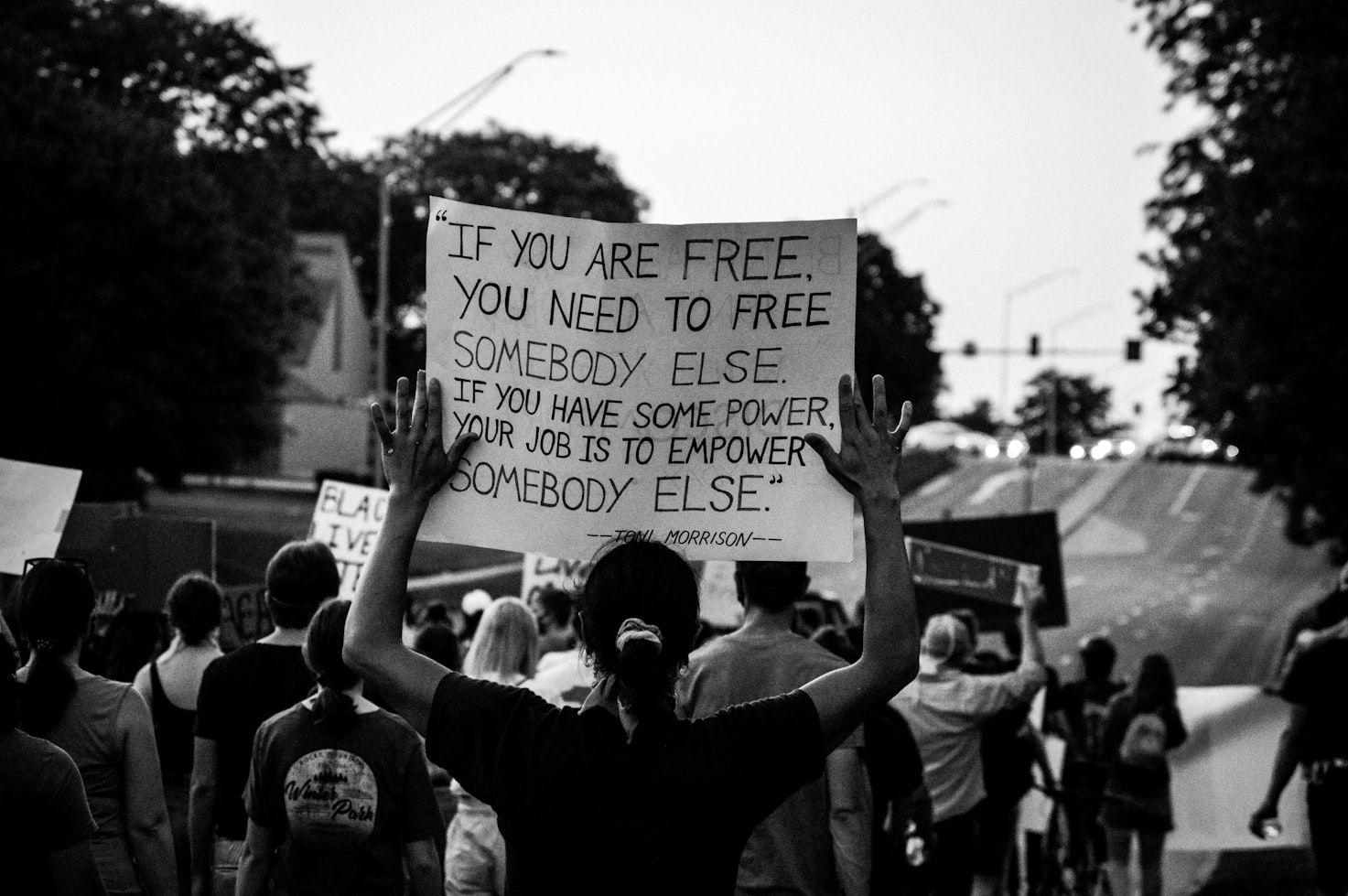 photo of a person holding a sign with a quote from Toni Morrison:  If you are free, you need to free somebody else. If you have some power, then your job is to empower somebody else.