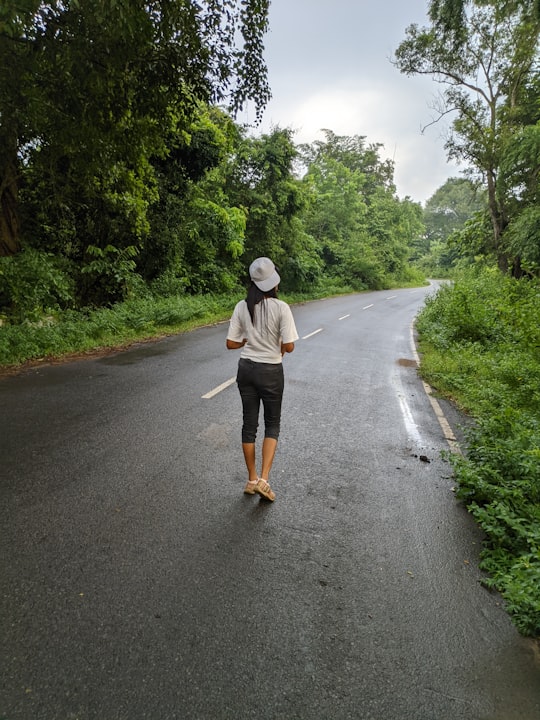 woman in white long sleeve shirt and black pants walking on gray asphalt road during daytime in Addateegala India