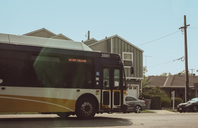 A public transit bus labeled '68 RIV College' is driving through a residential area. The bus is primarily yellow, black, and white, with the number 2881 displayed on it. There are houses in the background along with a few parked cars and telephone poles.