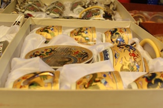 A set of ornately decorated porcelain teacups and saucers featuring colorful dragon motifs arranged neatly in a display box lined with white fabric.