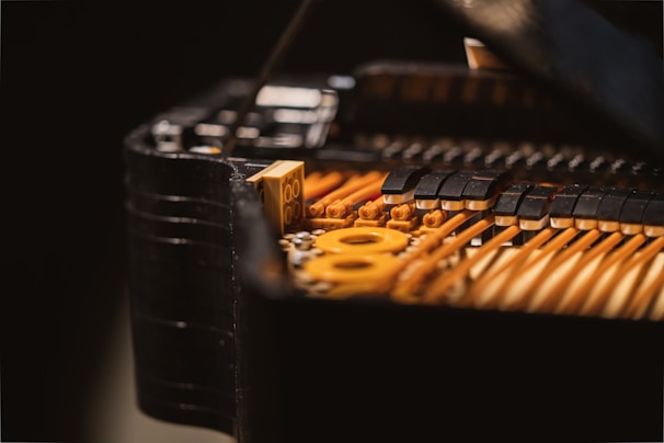 A close-up view of the internal mechanics of a piano, focusing on the strings and hammers. The image reveals intricate details of the instrument with brass-colored strings and black felted hammers. The lighting highlights the textures and craftsmanship.