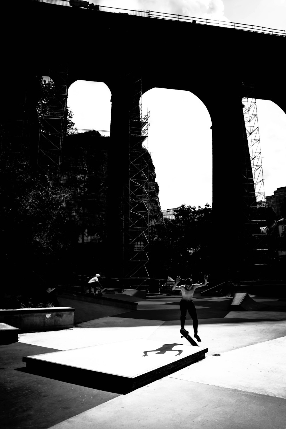 grayscale photo of woman walking on sidewalk near trees