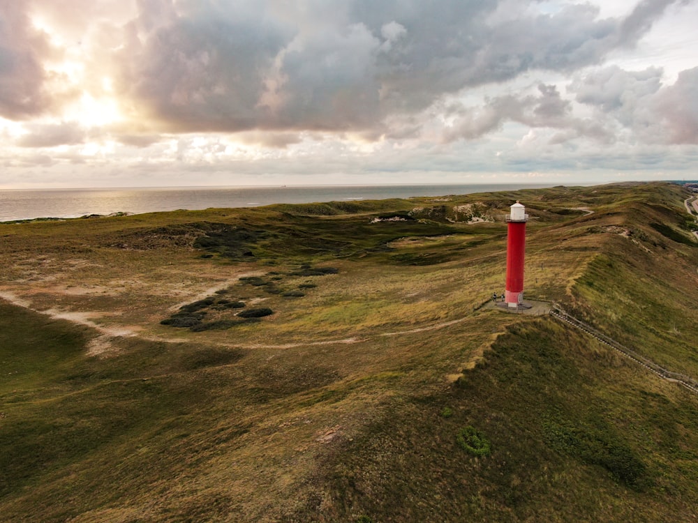 white and red lighthouse on green grass field under cloudy sky during daytime