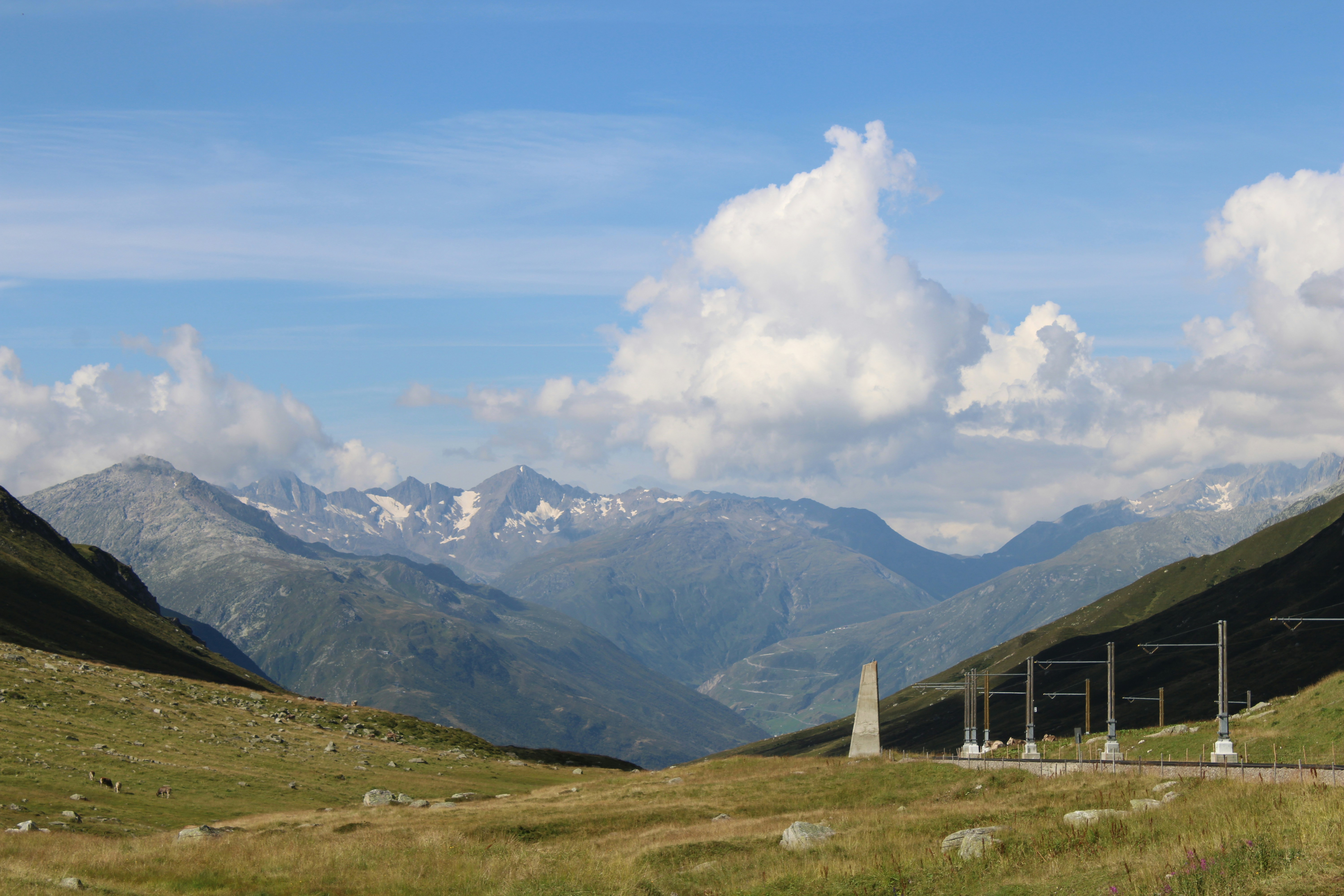 brown wooden house on green grass field near mountains under white clouds and blue sky during, 