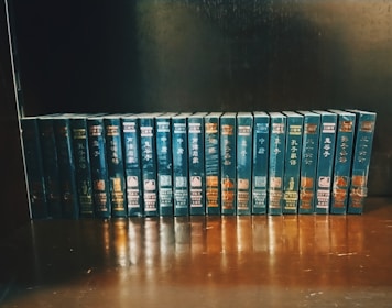A neatly arranged collection of books with identical dark blue covers and gold lettering sits on a wooden shelf. Each book is uniformly positioned, creating a visually appealing display.