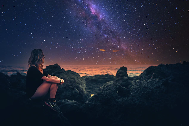 A confident woman looking thoughtfully at a glowing constellation map, symbolizing her journey to wealth and direction.