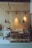 A cozy coffee shop interior with a wooden menu board on the wall, displaying options for specialty coffee, loose leaf tea, and hot chocolate. The counter has a glass display case filled with assorted pastries, and there are various coffee-making supplies and packaged goods arranged neatly. Overhead pendant lights hang, adding a warm atmosphere.