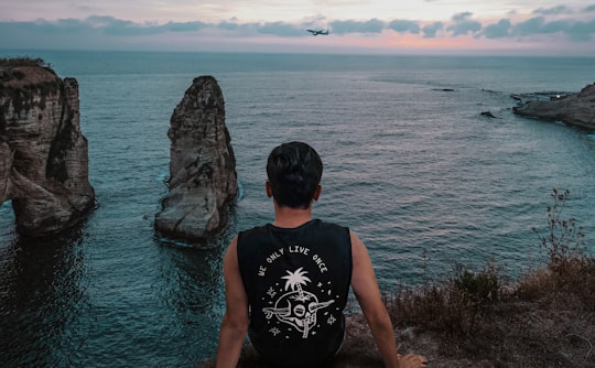 man in black tank top standing on rock near sea during daytime in Pigeons' Rock Lebanon