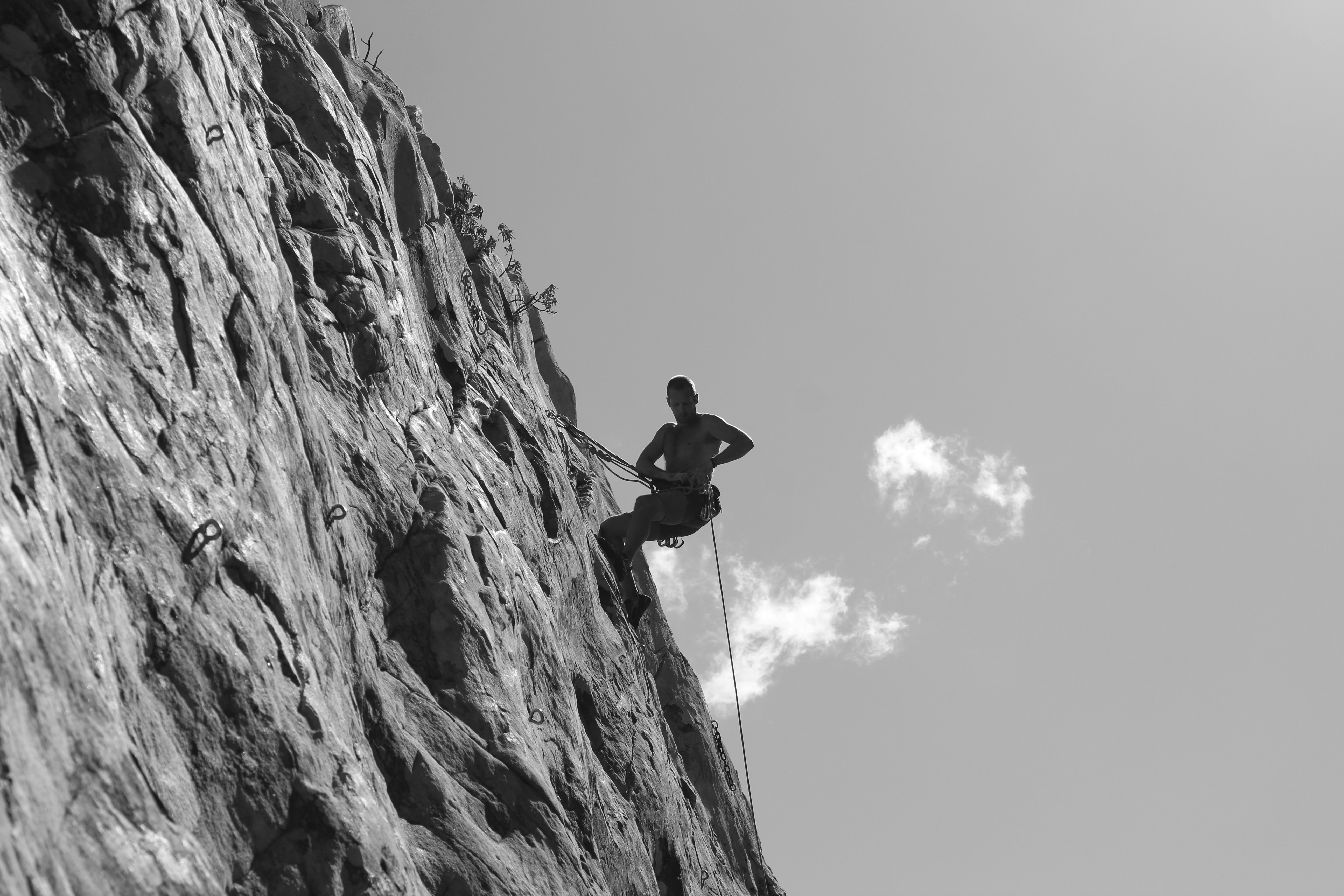 grayscale photo of man climbing on rock