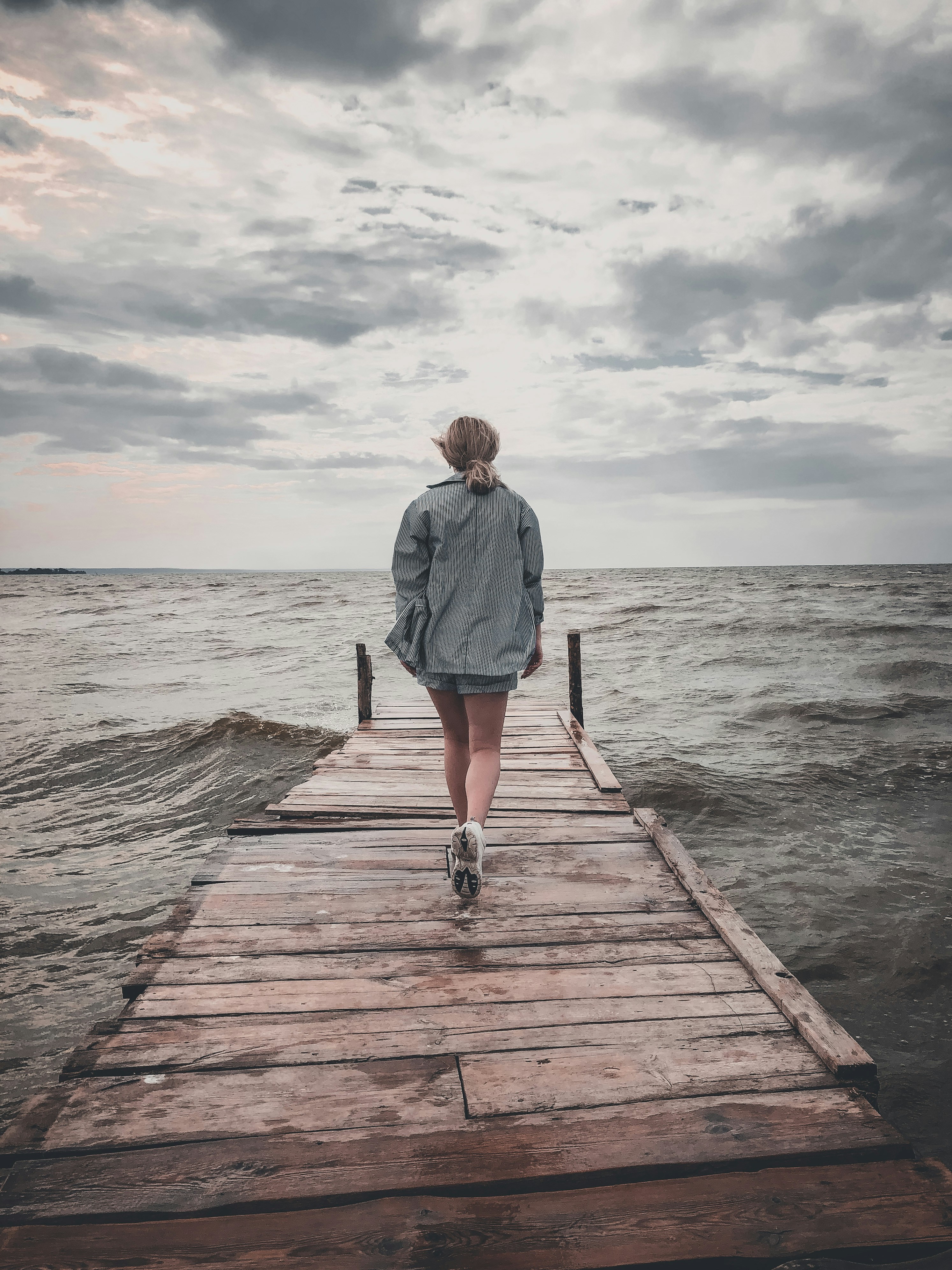 man in blue shirt and blue denim shorts walking on wooden dock during daytime
