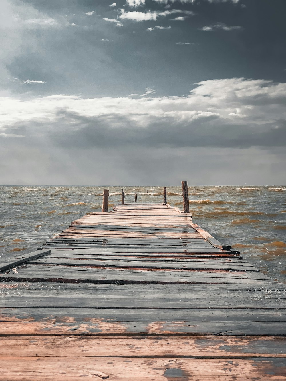 brown wooden dock on sea under white clouds during daytime